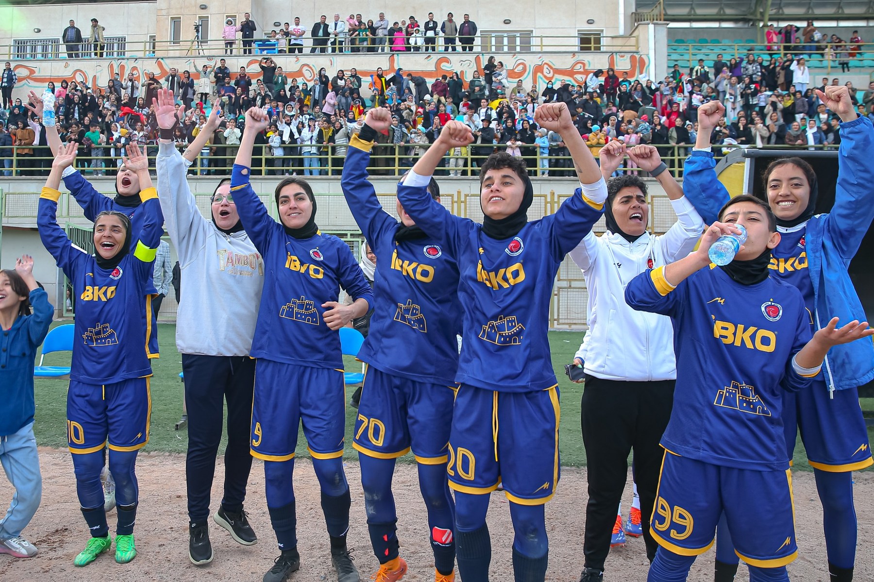 Bam Khatoon FC players celebrating in blue kits with supporters behind them